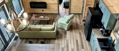 A compact, modern cabin with a wooden interior, a dining area, a sofa, a TV, and a kitchenette.
