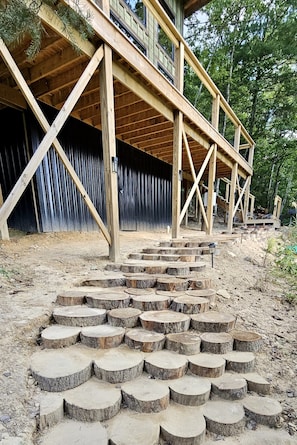 A wooden staircase leading to a wooden deck with a metal fence in the background.