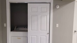 A laundry room with a washing machine and dryer, a door, and a light switch on the wall. - Cozy and Comfortable 1 bedroom (Belgium)