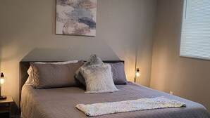 A bedroom with a bed, two bedside lamps, a wall art piece, and a window with blinds. - Cozy and Comfortable 1 bedroom (Belgium)