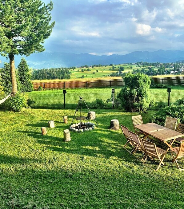 A grassy outdoor area with a fire pit, wooden chairs, and a table. - Mountain Cozy House in Tatras With Stunning View (Poronin)