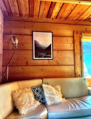 A wooden cabin interior with a leather couch, a framed picture on the wall, and a lamp.