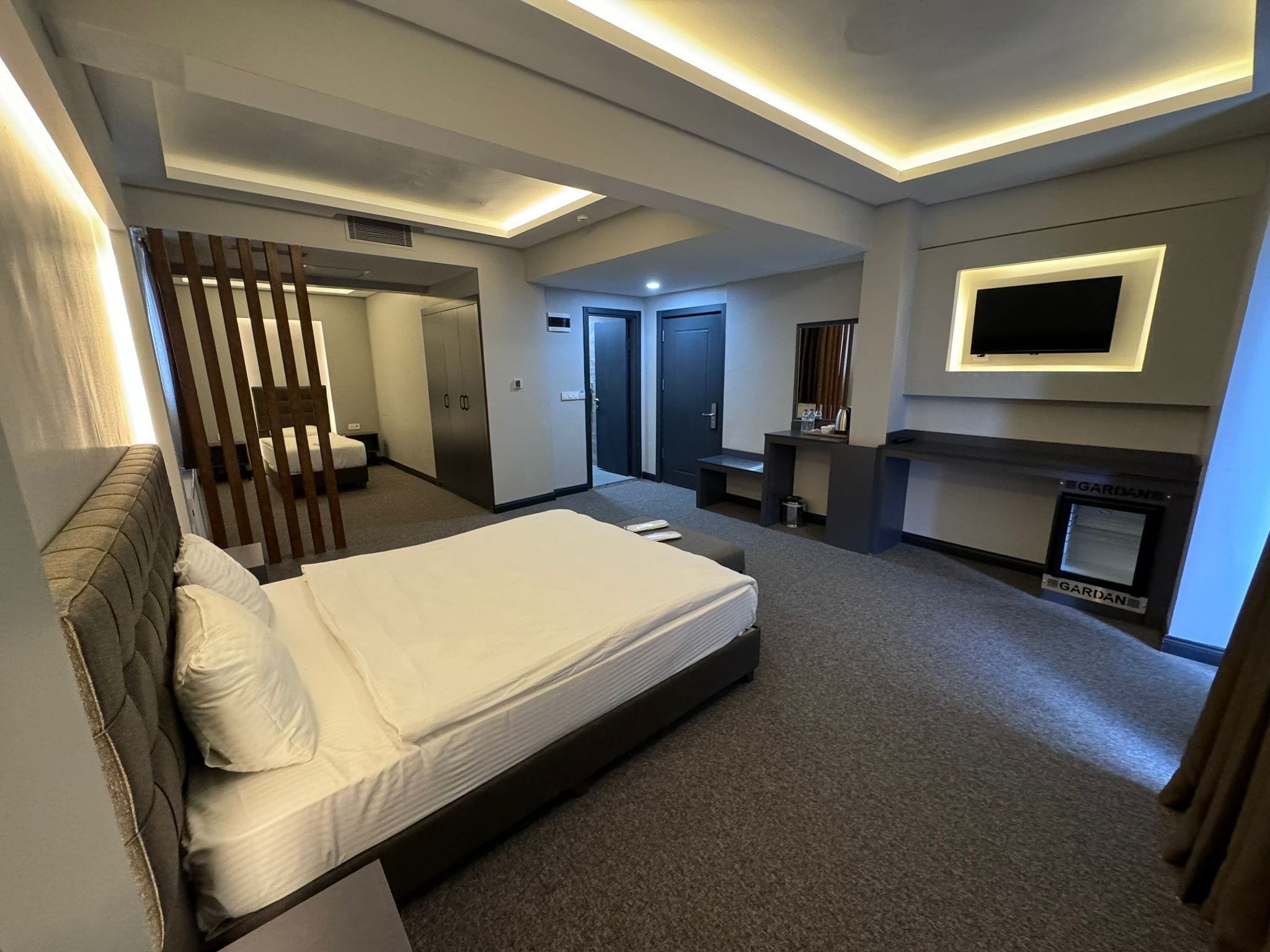 Una habitació d'hotel moderna amb un llit gran, un televisor fixat a la paret, una llar de foc i un bany separat.