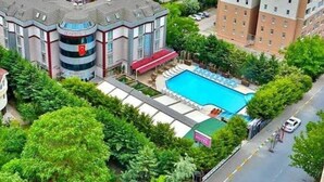 A hotel with a swimming pool surrounded by lush greenery, a red-roofed building, and a parking area. - Gardan Hotel (Istanbul)