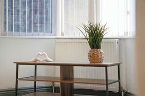 A room with a white radiator, a wooden table with a heart-shaped object, and a potted plant.