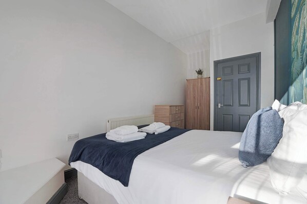 A bedroom with a bed, a dresser, a door, and a radiator.