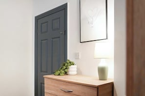 A room with a closed door, a wall-mounted light, a small potted plant, and a framed picture.