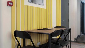 Une petite salle de réunion avec une table et quatre chaises, une boîte rouge contenant du matériel de premiers secours, et une porte située sur le côté droit.