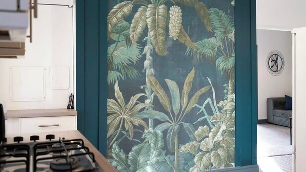 A kitchen with a gas stove, a cabinet, and a wall with a tropical plant mural.