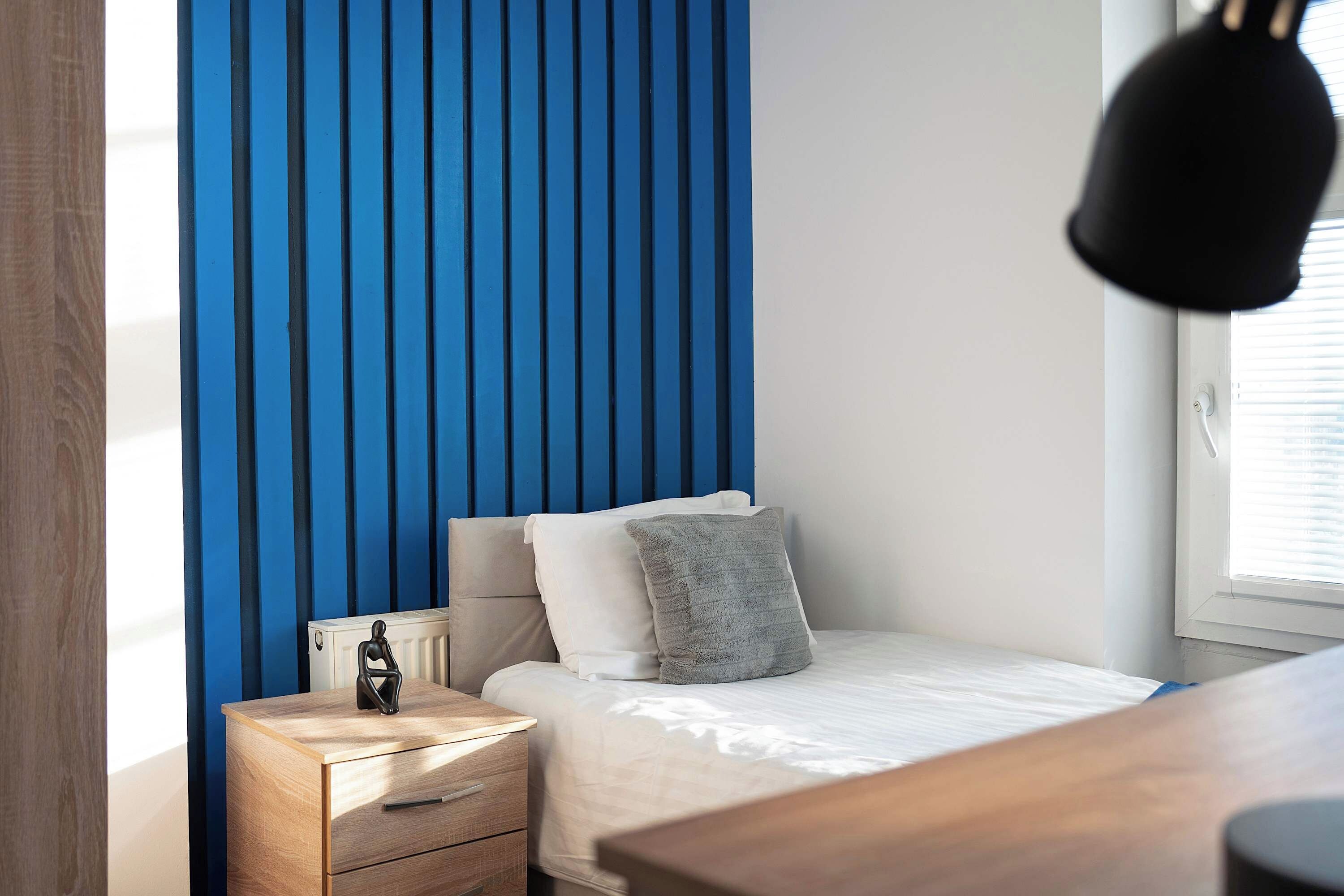 Une chambre à coucher comprenant un lit, une table de chevet, une commode et une fenêtre avec des stores.