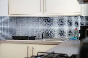 Et køkken med hvide skabe, et flisebeklædt bagpanel og en vask med armatur.