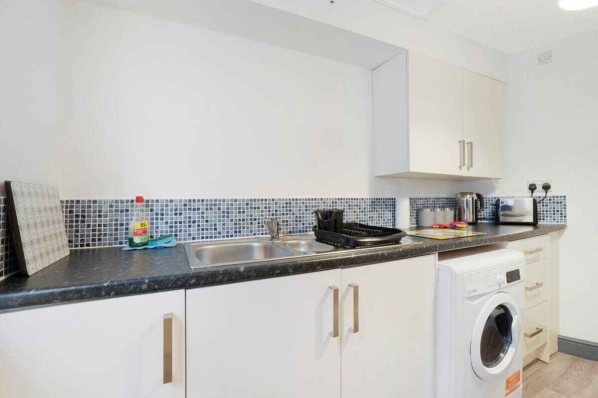 A kitchen with white cabinets, a washing machine, and a tiled backsplash.