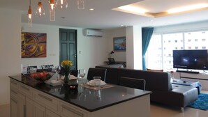 Una sala de estar moderna con un televisor grande, un sofá y una zona de comedor con una mesa preparada para dos personas.