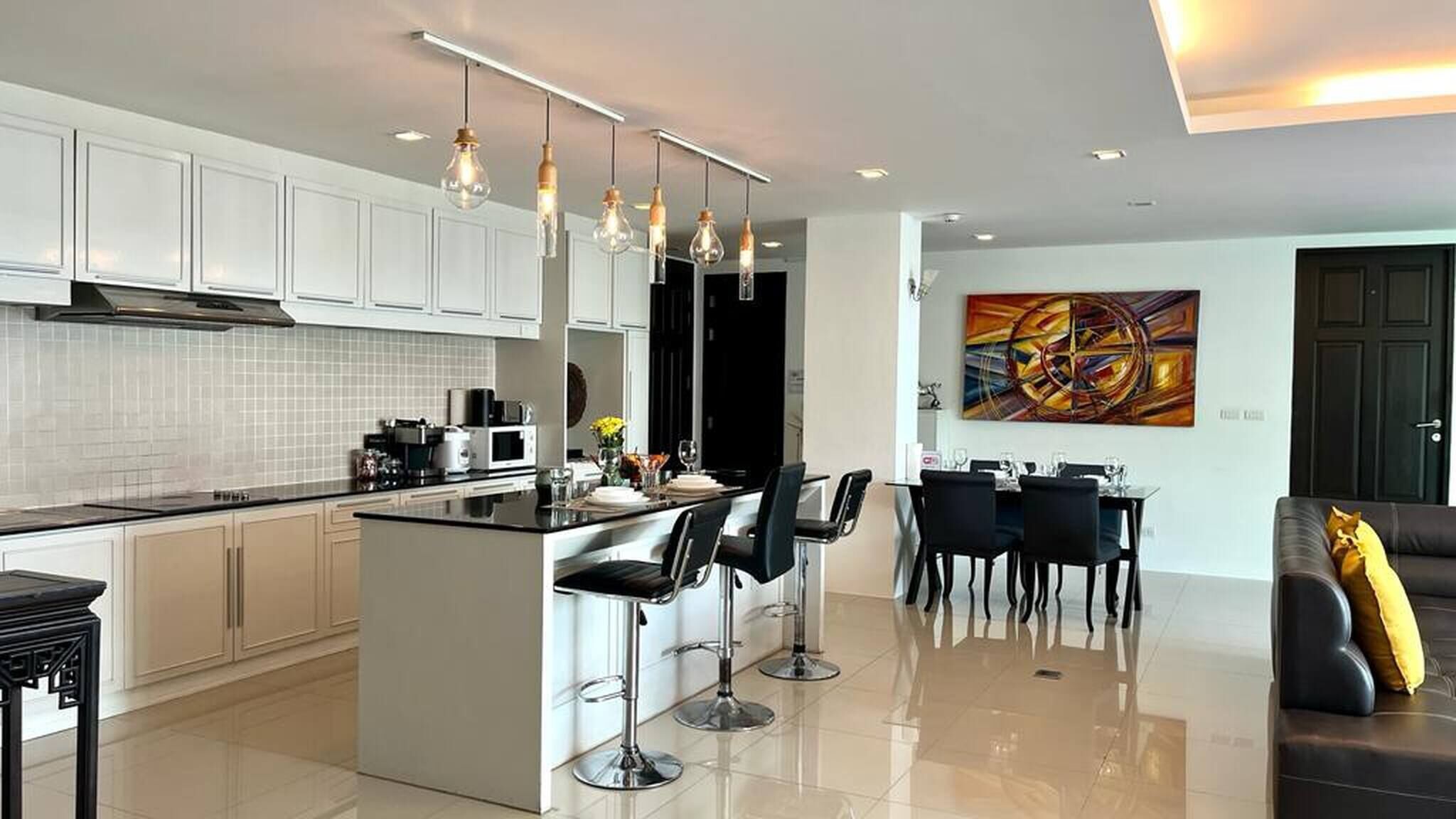 A modern kitchen with white cabinets, a central island with bar stools, and pendant lighting.