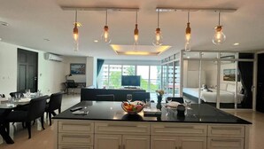 Una cocina moderna con una isla central, comedor y sala de estar con televisión y vista al balcón.