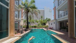 Una piscina con una persona nadando, rodeada de edificios y palmeras.