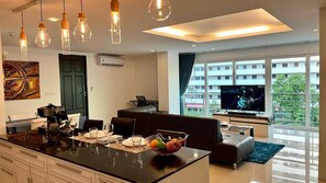 Une cuisine moderne avec un îlot central, un coin repas avec un canapé et un salon équipé d’un téléviseur.