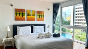 Habitación de hotel con una cama grande, dos mesitas de noche, vistas a una piscina y tres cuadros en la pared.