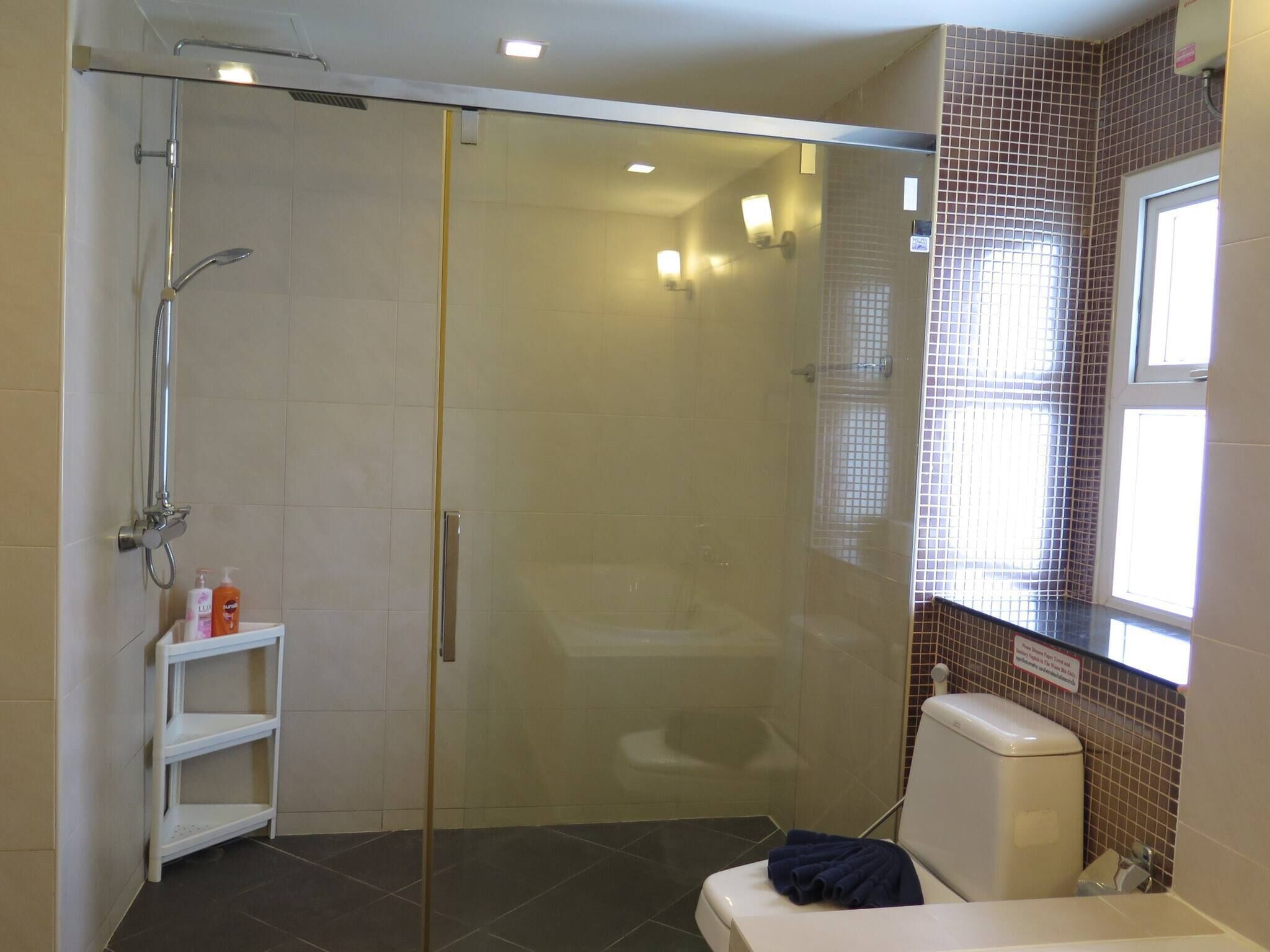 Une salle de bain moderne avec une douche à parois de verre, des toilettes blanches et une petite étagère contenant des articles de toilette.