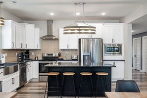 A modern kitchen with white cabinetry, stainless steel appliances, a central island with bar stools, and a hanging light fixture. - 5BR Hot Tub Steps to Indoor Pool Sleeps 16 (Hollister)