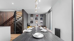 A modern dining area with a long table set for a meal, a staircase, and a wall decorated with various framed pictures.