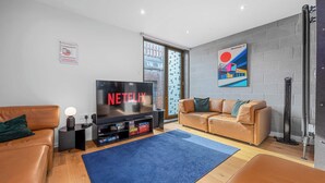 A modern living room with a flat-screen TV, leather sofas, a blue rug, and a cityscape painting on the wall.