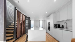 A modern kitchen with a central island, wooden flooring, and a staircase with a black and brown design.