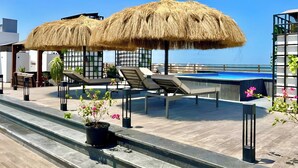 A rooftop pool area with lounge chairs, a thatched umbrella, and a view of the sea. - Imperial Resort Hurghada - New Roof Top Pool! (Hurghada)
