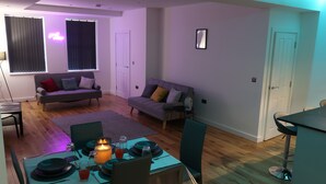 Un salon moderne avec un coin repas, comprenant un canapé, une table dressée pour deux personnes et un néon mural.