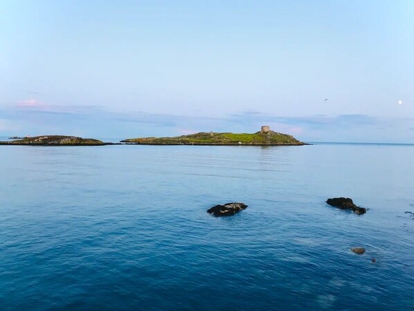 A coastal scene with calm blue waters, a small island with a building, and a clear sky.