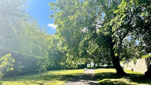 A gravel path leading through a grassy area with trees and a stone wall in the background.