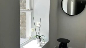 A room with a window, a potted orchid, a round mirror, and a stool.