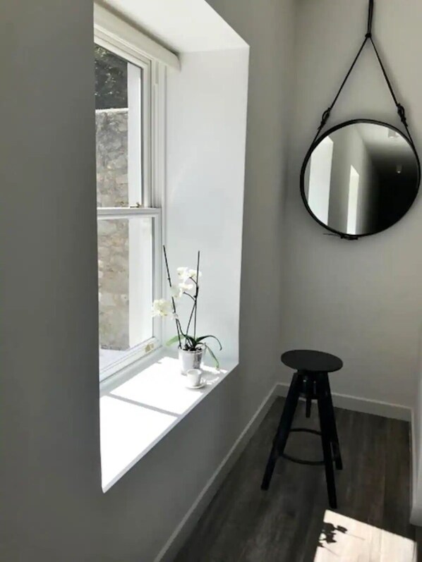 Una habitació amb finestra, orquídia en testos, mirall rodó i un tamboret.