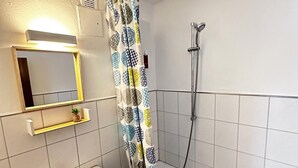 A bathroom with a white sink, a mirror, a shower with a patterned curtain, and a tiled wall. - Moderne Ferienwohnungen und -zimmer in Kleve (Kleve)