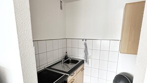 A compact kitchen with white tiles, a black stove, a sink, and a trash bin. - Moderne Ferienwohnungen und -zimmer in Kleve (Kleve)