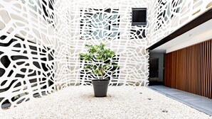 A modern building with a unique white perforated facade, a central potted plant, and a wooden slatted wall on the right. - Cathedral Apartment Welcome Wheelchairs (Sevilla)