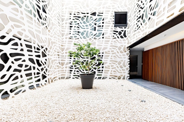 A modern building with a unique white perforated facade, a central potted plant, and a wooden slatted wall on the right.