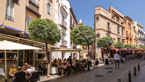 A bustling outdoor café with tables and chairs, surrounded by historic buildings with balconies and trees. - Cathedral Apartment Welcome Wheelchairs (Sevilla)