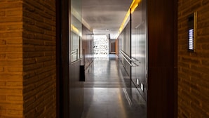 A modern hotel corridor with brick walls, metal railings, and a patterned wall at the end. - Cathedral Apartment Welcome Wheelchairs (Sevilla)