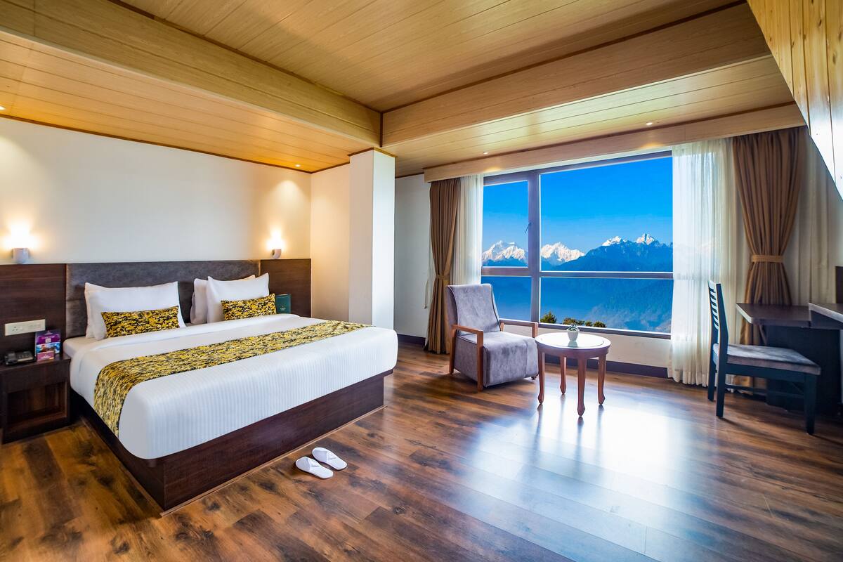 Quarto de hotel com uma cama grande, uma escrivaninha, uma cadeira e vista para as montanhas.