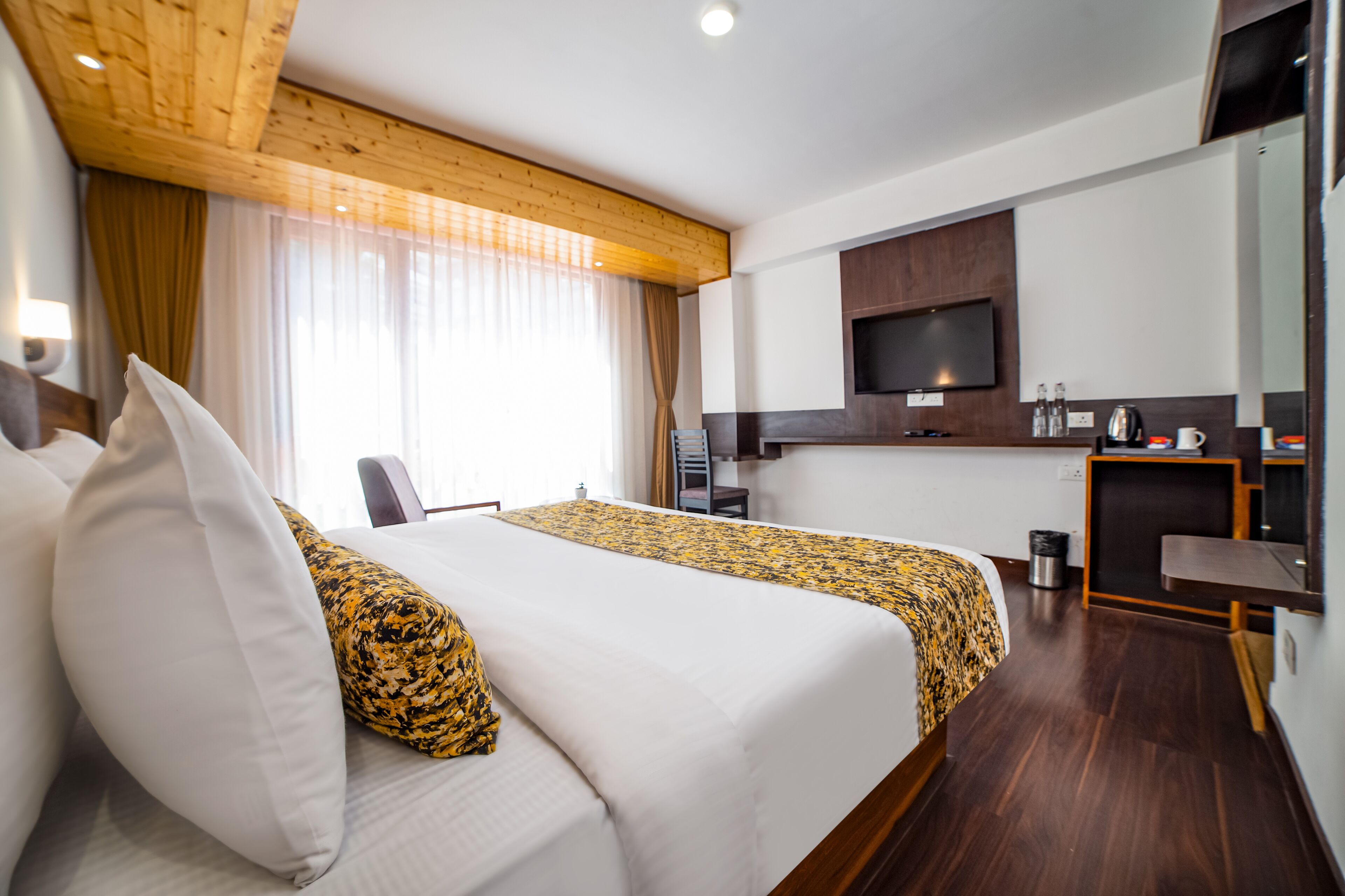 A hotel room with two beds, a TV, a desk, and a small kitchenette.