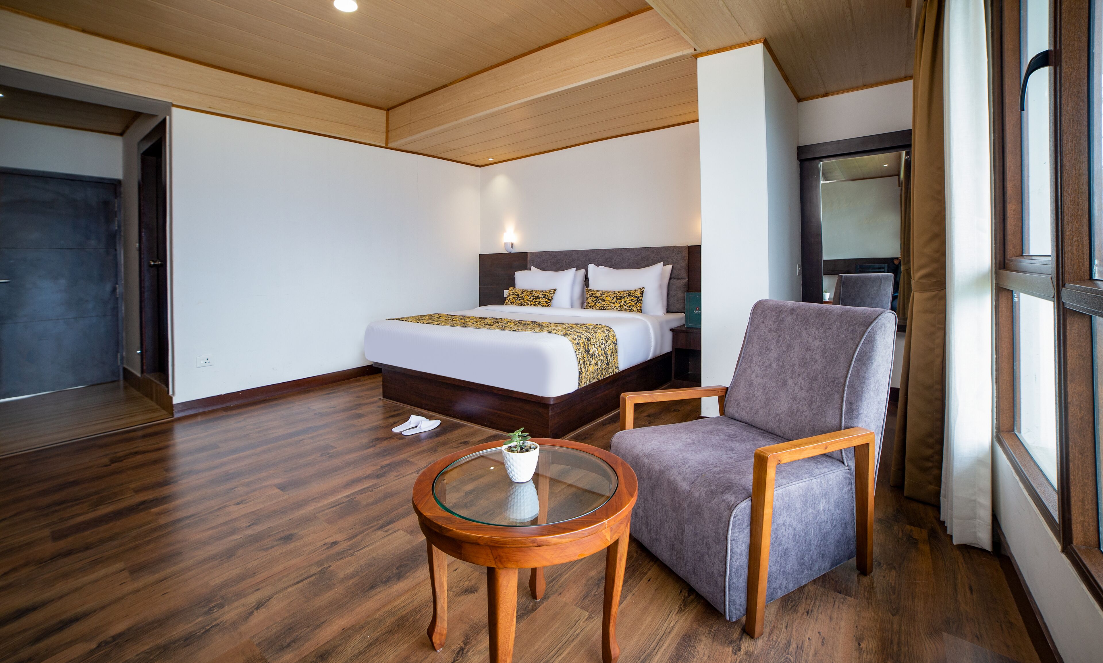 A hotel room with a bed, a chair, a small table, and a window.