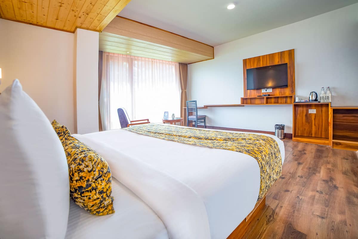 Quarto de hotel com uma cama grande, uma TV presa à parede, uma escrivaninha de madeira e uma janela com cortinas.