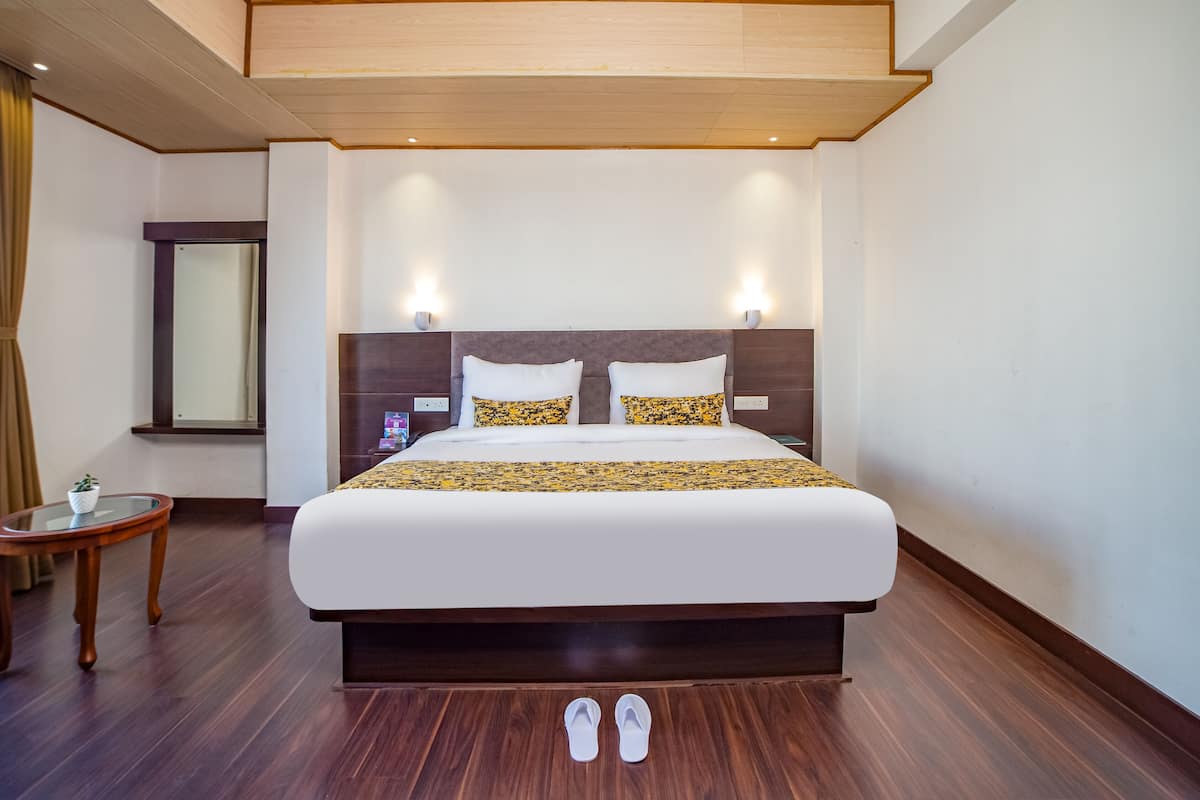Quarto de hotel com uma cama grande, mesa de cabeceira, espelho e uma pequena mesa com uma planta.