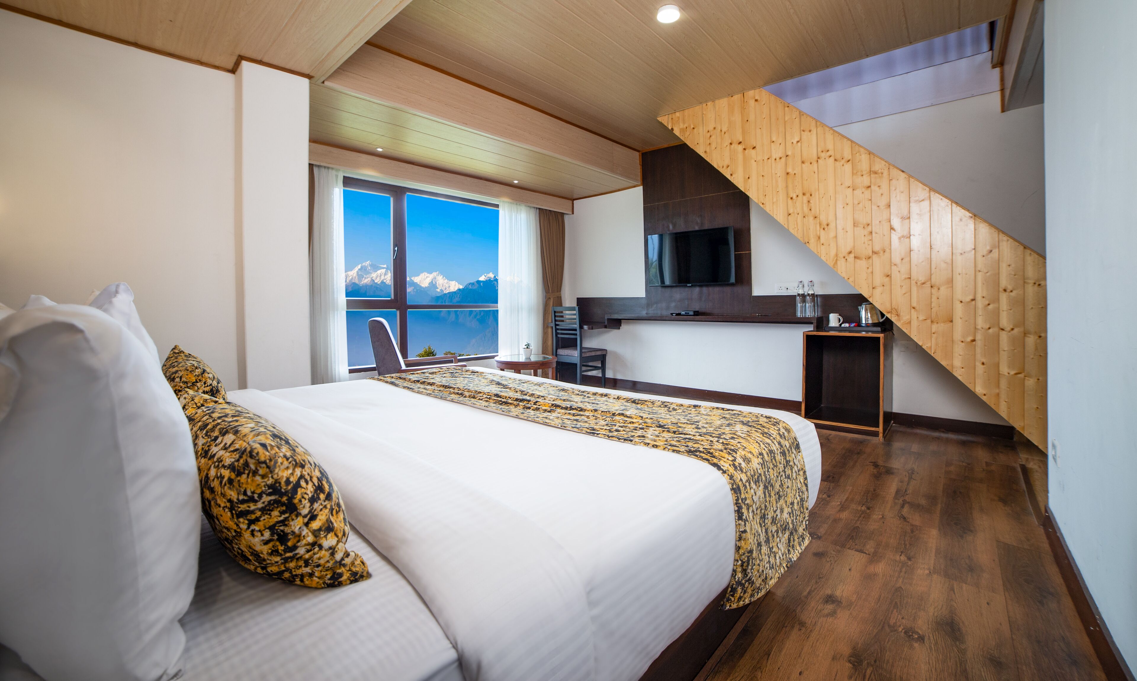 Habitación de hotel con cama, escritorio, silla, televisión y vistas a las montañas.