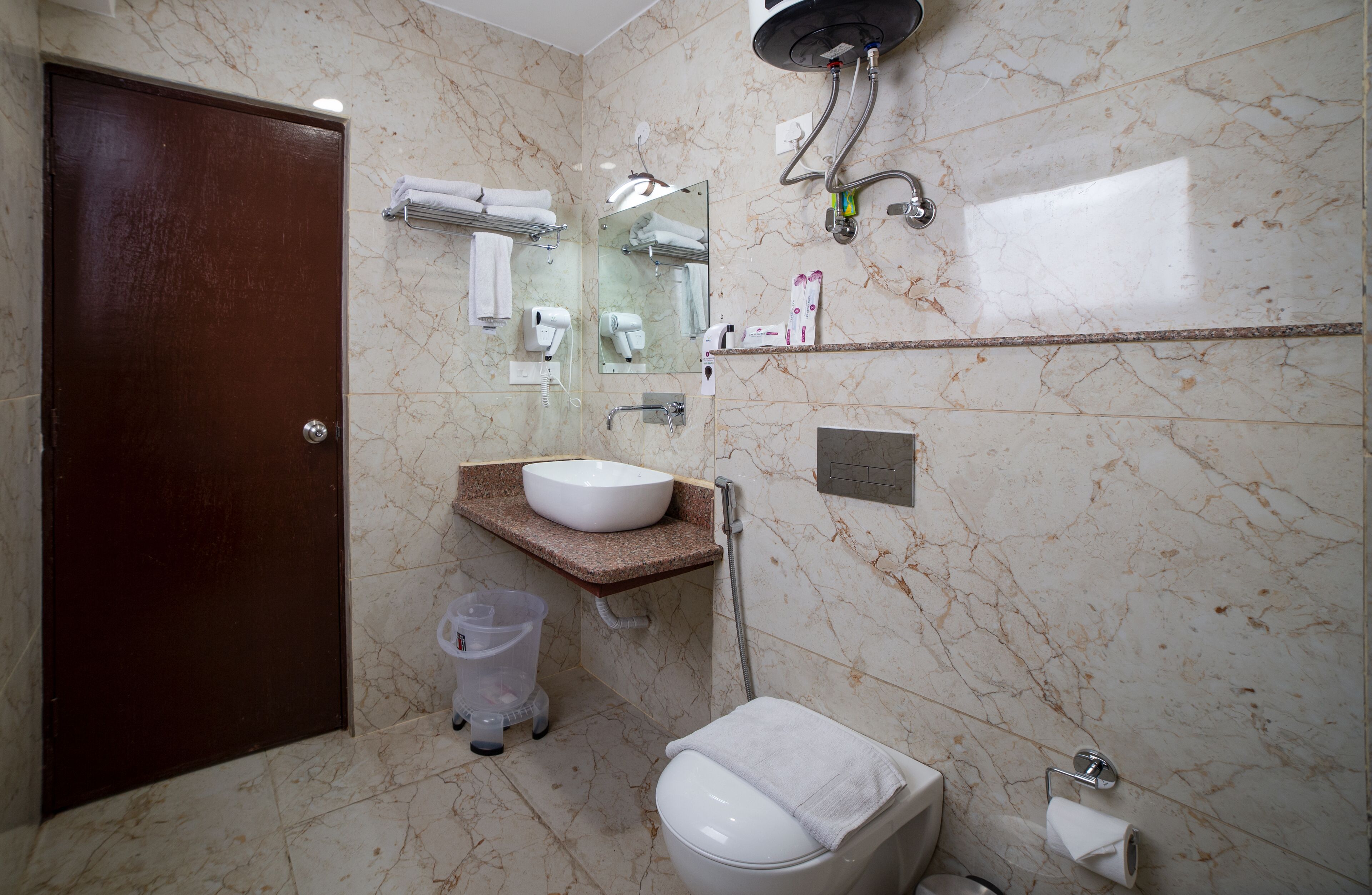Une salle de bain avec un mur en marbre, un lavabo, des toilettes, une douche et un miroir.