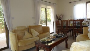 A living room with a sofa, a coffee table, and a dining area with chairs and a table. - Gracelands Emba Cypriot Village Life (Emba)