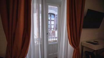 Een deuropening met witte gordijnen, een klein tafeltje met een boek, en uitzicht op een balkon met een hekwerk.