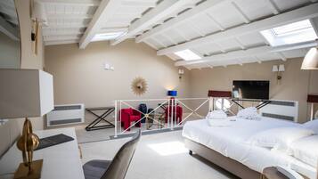 Habitación de hotel con cama, escritorio, silla, televisión y balcón con sillas rojas y un adorno tipo sol.