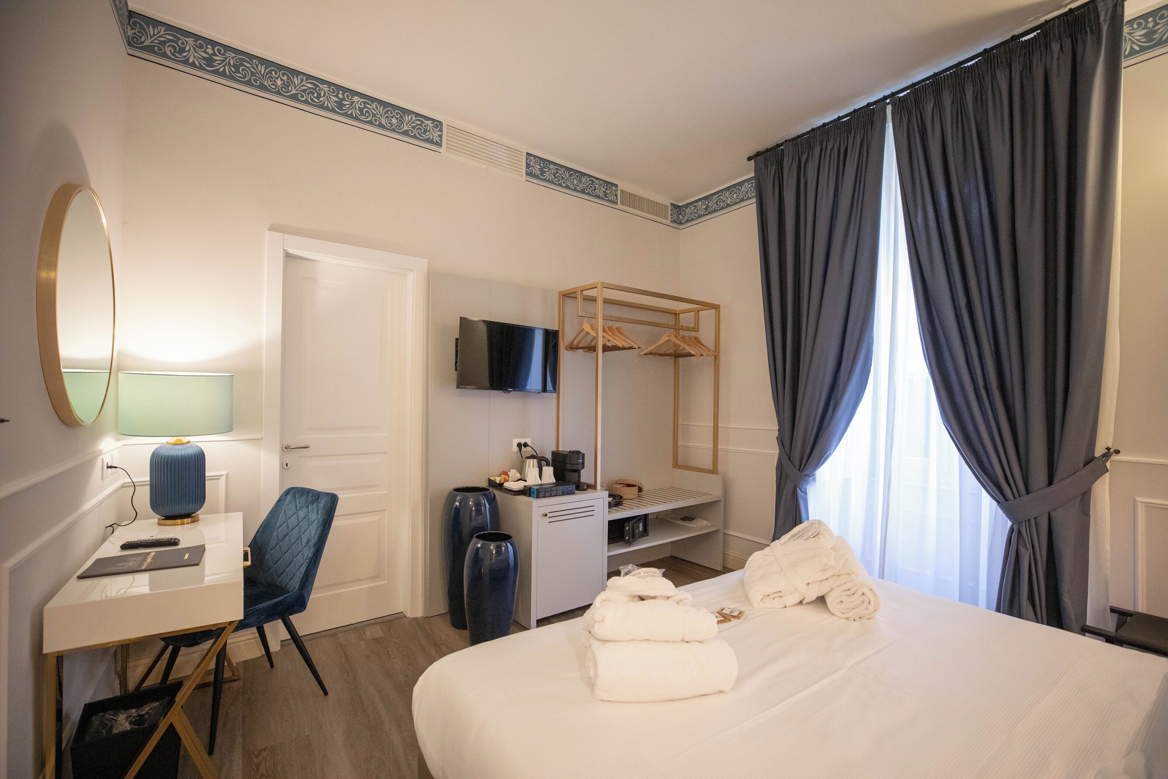 A hotel room with a bed, a desk with a chair, a TV, a wardrobe, and a window with curtains.